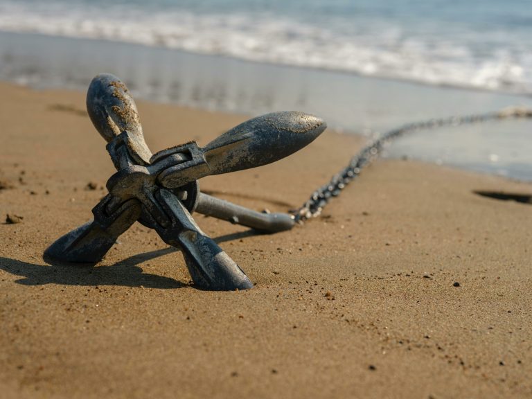 Close-up view of a metallic anchor resting on a sandy beach near the ocean shore.